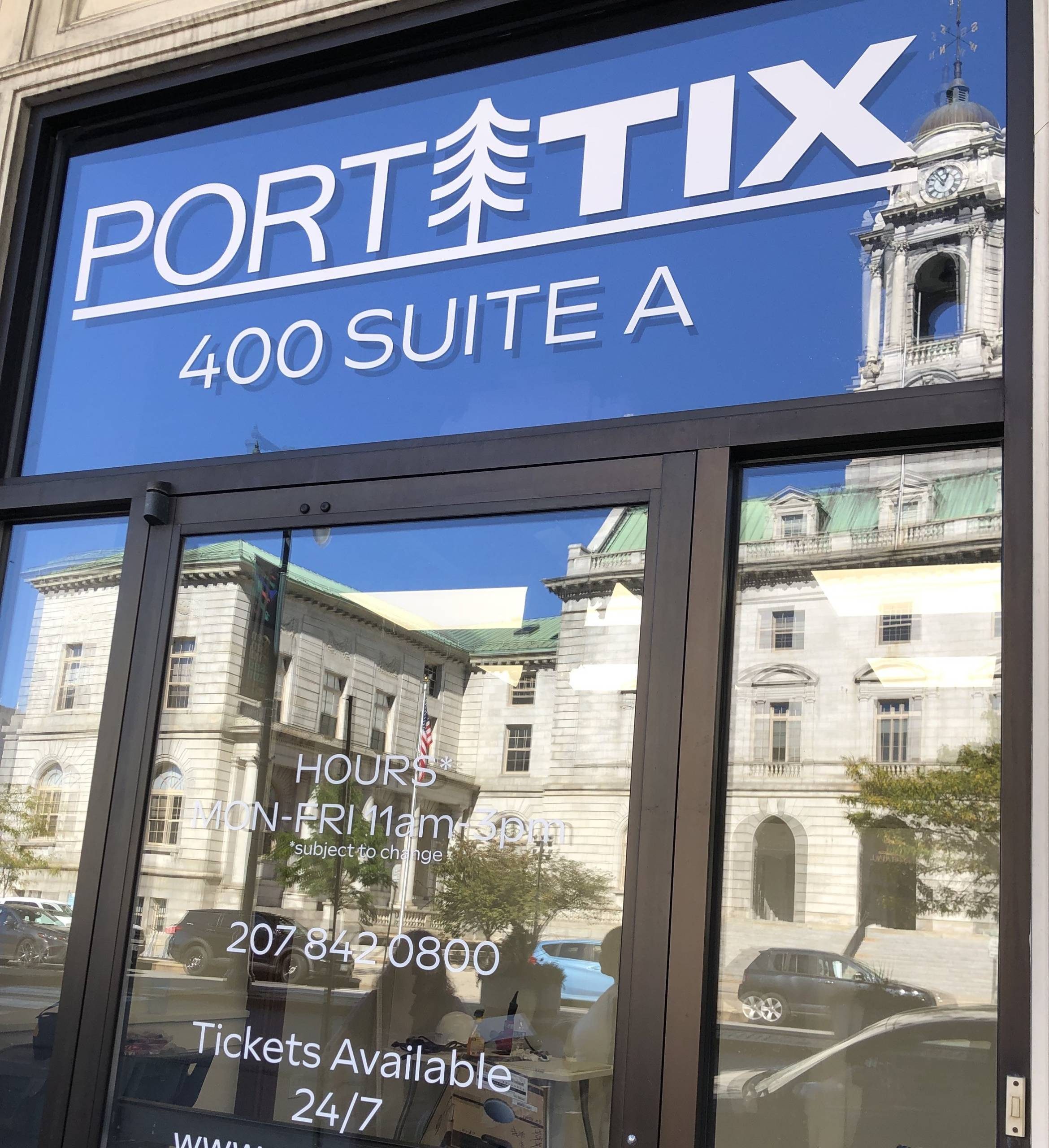 PortTIX's storefront at 400 Congress St Suite A. Visible is the porttix logo and 400 suite a printed on the window, and portland city hall reflected in the window.